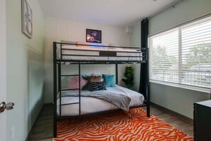 Ein Schlafraum mit Etagenbetten, einem zebra-gemusterten Teppich, einer Pflanze und einem Fenster mit Jalousien.
