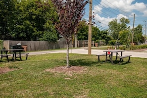 A picnic area with two tables and benches, surrounded by grass and trees.
