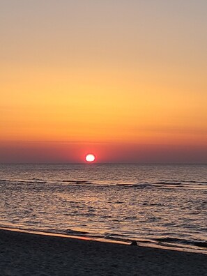 Enjoy a serene sunset over the calm sea, with the sun setting near the horizon.