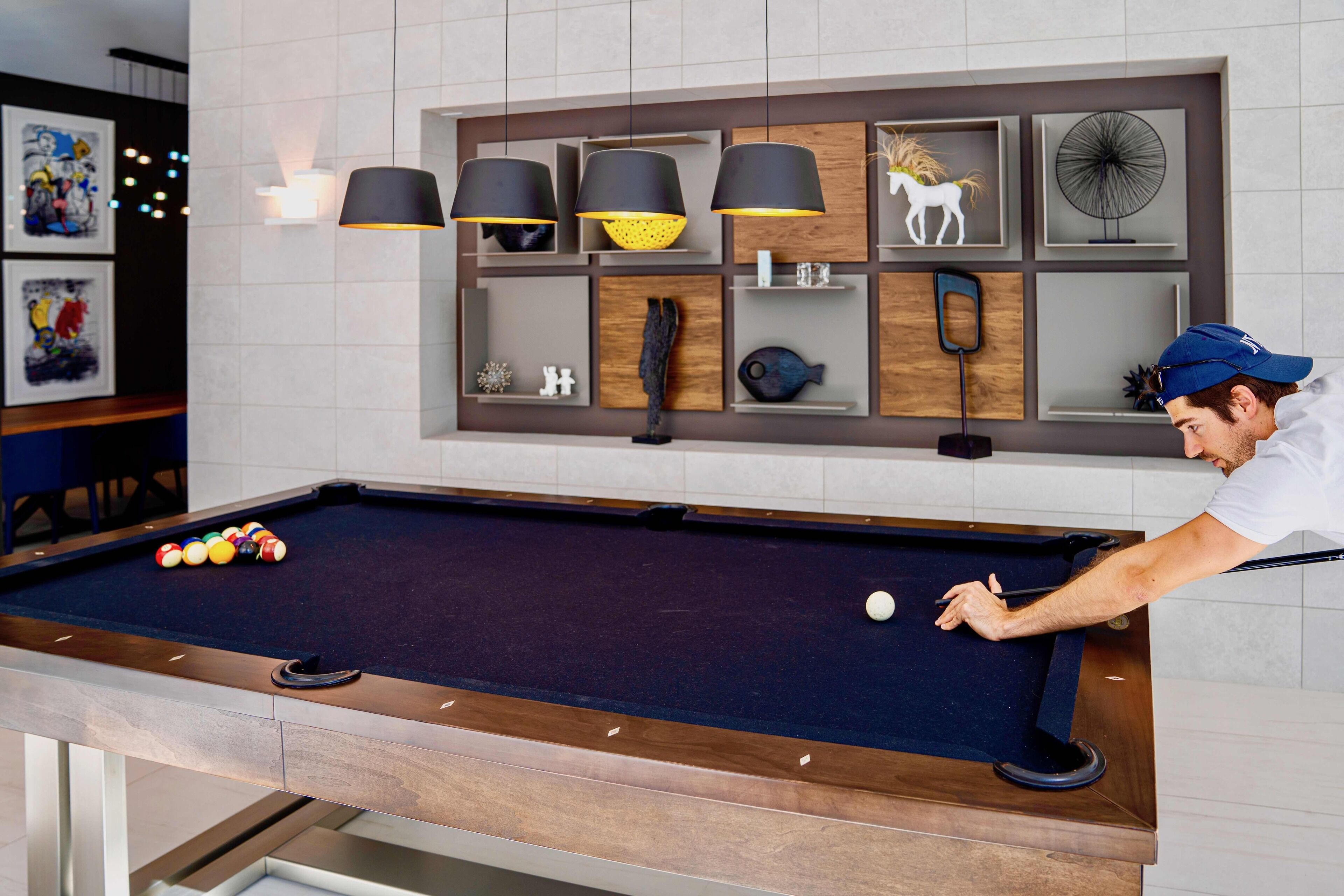 A pool table with balls, a person playing, and a wall with shelves and artwork.
