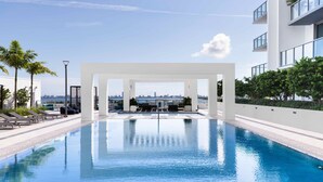 En swimmingpool med udsigt til en bysilhuet, omgivet af palmer og moderne bygninger.