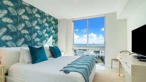 Een slaapkamer met een bed, een bureau en een groot raam met uitzicht op de stad.