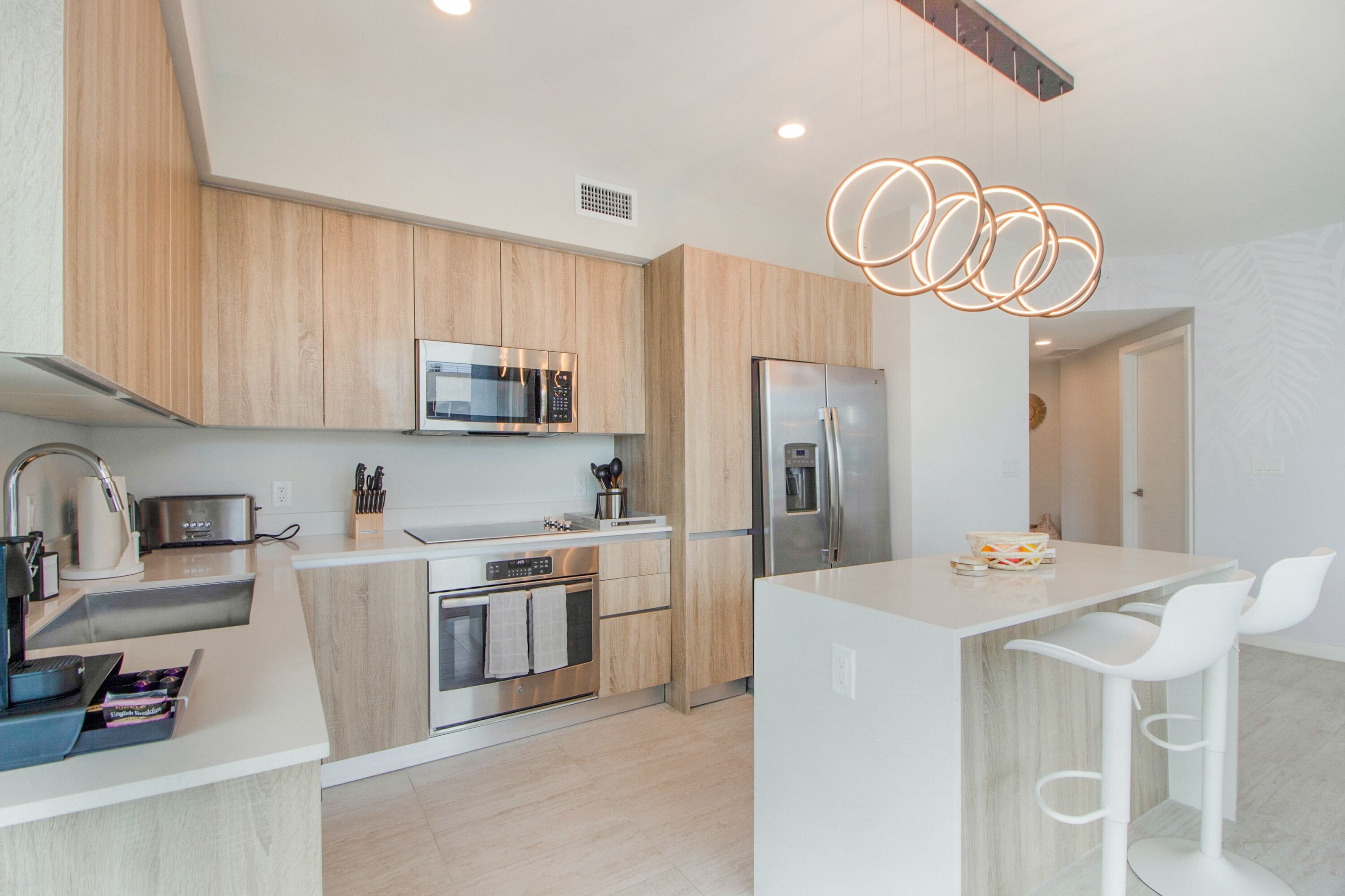 A modern kitchen with wooden cabinets, stainless steel appliances, and a central island with white bar stools.
