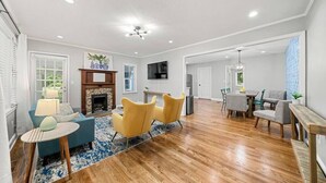 A spacious living room with hardwood floors, a fireplace, and a dining area with a table and chairs. - Serene 3BR home in Historic Downtown Norcross (Norcross)