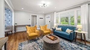 A living room with a blue sofa, two yellow armchairs, a round wicker coffee table, and a wooden floor. - Serene 3BR home in Historic Downtown Norcross (Norcross)