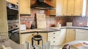 Une cuisine avec des meubles de rangement en bois, une hotte aspirante noire, un plan de travail sur lequel se trouvent une machine à café, un grille-pain et une miche de pain sur une assiette.