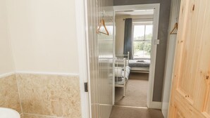 Un couloir étroit mène à une chambre à coucher qui contient un lit, une fenêtre avec des rideaux et une porte en bois.