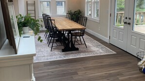 Un comedor amplio con mesa y sillas de madera, una araña y ventanas grandes.