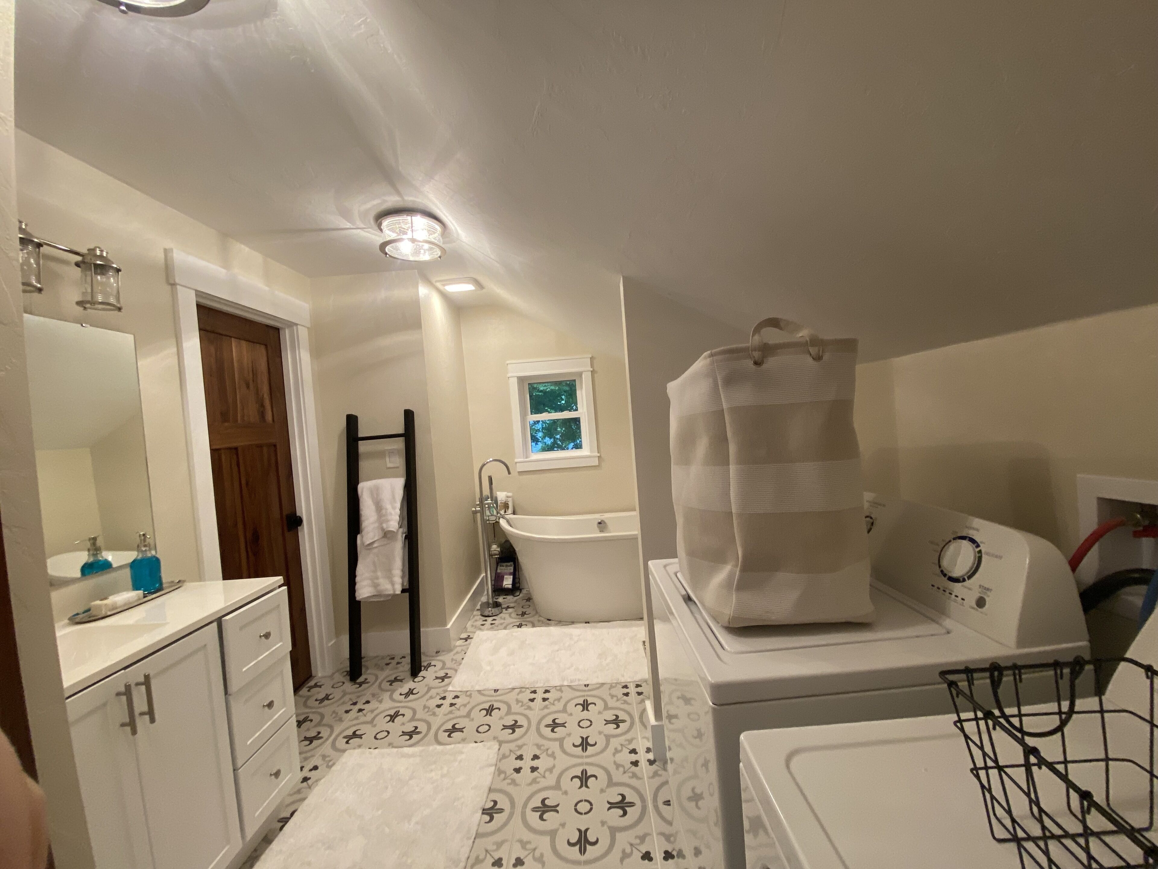 A bathroom with a bathtub, a toilet, a sink, and a mirror. There is a towel rack and a window with a view of trees.