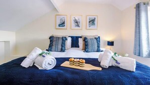 Une chambre d’hôtel avec un grand lit, une literie bleue, trois œuvres d’art encadrées accrochées au mur et un plateau en bois contenant des pâtisseries.
