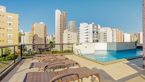 A rooftop pool area with lounge chairs, a swimming pool, and a cityscape view.