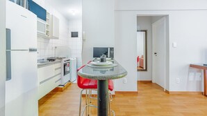 A modern kitchen with white cabinets, a granite countertop, a red chair, and a microwave.