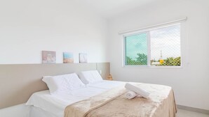 A neatly made bed with a white comforter and a beige blanket, a small bedside lamp, and three framed pictures on the wall. - GB37 Excellent Apt 2 Suites in Guarajuba (Camaçari)