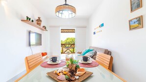 A dining area with a glass table, wicker placemats, and a variety of seafood. There are two wooden chairs, a wicker bench, and a television on the wall. - GB37 Excellent Apt 2 Suites in Guarajuba (Camaçari)