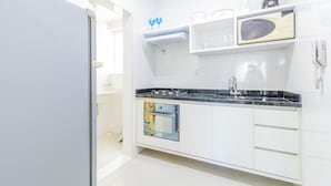 A modern kitchen with white cabinets, a black countertop, a built-in oven, a microwave, and a blender on the shelf. - BR03 2 Bedroom Apt 200m from Porto Barra Beach (Salvador)