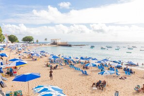 A beach with numerous blue umbrellas, sandy shore, and a few boats in the water. - BR03 2 Bedroom Apt 200m from Porto Barra Beach (Salvador)