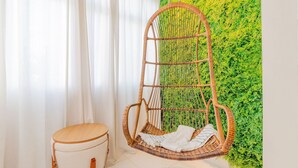 A wicker hanging chair with a cushion, a round wooden stool, and a green vertical garden wall. - VT06 Bedroom/Living Room Apartment - Vilas do Atlântico (Lauro de Freitas)