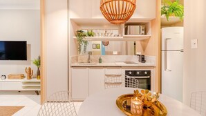 A modern kitchen with white cabinetry, a built-in microwave, and a stainless steel refrigerator. - VT06 Bedroom/Living Room Apartment - Vilas do Atlântico (Lauro de Freitas)