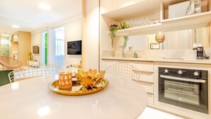 A modern kitchen with white cabinetry, a built-in oven, and a dining area with a round table and chairs. - VT06 Bedroom/Living Room Apartment - Vilas do Atlântico (Lauro de Freitas)