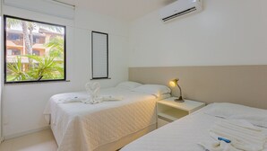 Hotelkamer met twee bedden, een raam met uitzicht op palmbomen, een airconditioner en een bedlampje.