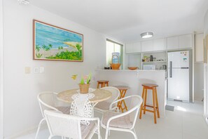 Una cucina con mobili bianchi, un frigorifero e un'area pranzo con sedie in vimini e un tavolo.