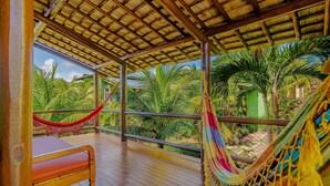 A wooden deck with a hammock and a bed, overlooking a tropical garden with palm trees.