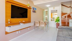 Un salon moderne avec un téléviseur fixé au mur, un coin repas avec une table et des chaises, et un escalier menant à un autre niveau.