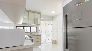 Une cuisine moderne dotée d’un réfrigérateur en acier inoxydable, de meubles blancs et d’une fenêtre laissant entrer la lumière naturelle.