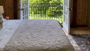 Un dormitorio con una cama grande, un ventilador de techo y vistas a un paisaje verde a través de puertas abiertas.