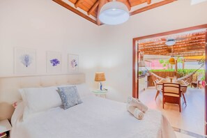 Quarto com cama, mesa de cabeceira, luminária e vista para uma área de refeições ao ar livre.
