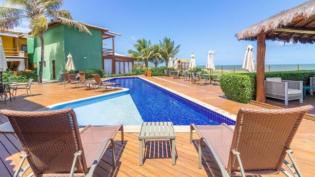 A pool area with lounge chairs, a small table, and umbrellas. - IT27 Village 3 Suites, Pé na Areia - Itacimirim (Camaçari)
