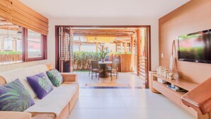 A modern living room with a sofa, TV, and dining area. - IT27 Village 3 Suites, Pé na Areia - Itacimirim (Camaçari)