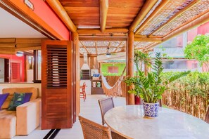 Uma área de estar acolhedora ao ar livre, com mesa redonda e cadeiras de vime, uma rede e um vaso de planta.