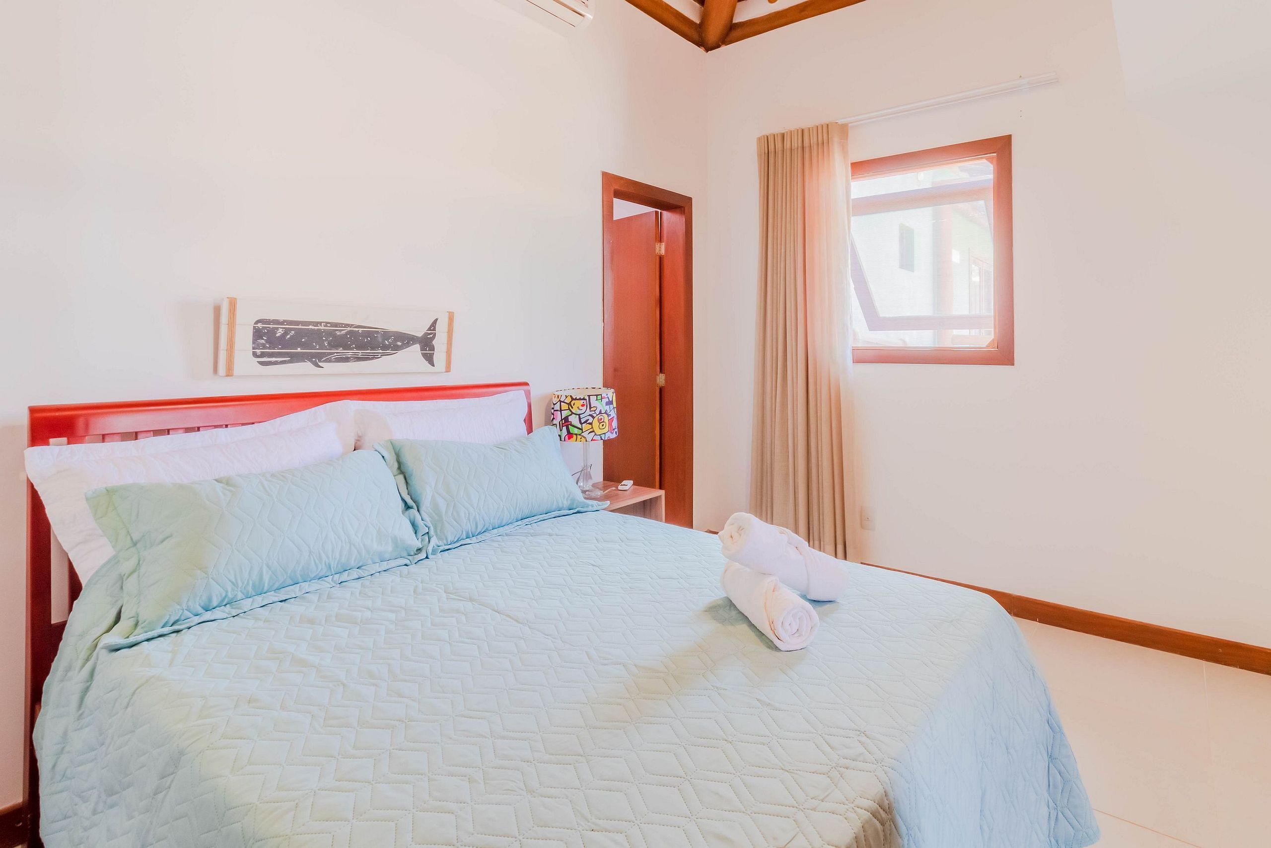A neatly made bed with a quilted cover, a wooden headboard, and a window with curtains.
