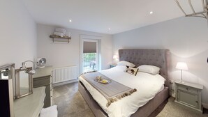 A bedroom with a large bed, bedside tables, a mirror, a radiator, and a window. - Private and Unique Cottage Close to Sheffield (Dronfield)