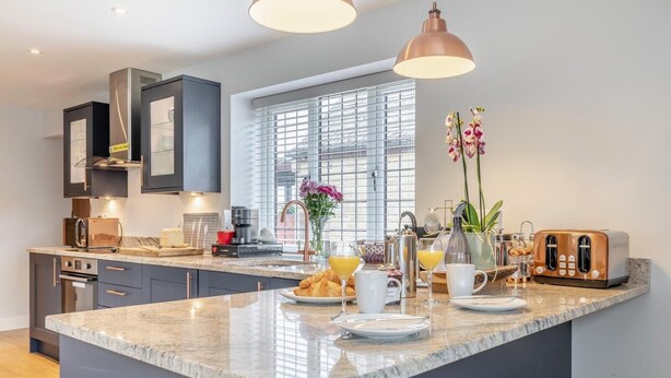 A modern kitchen with a central island, built-in appliances, and a large window. - Private and Unique Cottage Close to Sheffield (Dronfield)
