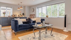 A modern living room with a blue sofa, a glass coffee table, and a kitchen area in the background. - Private and Unique Cottage Close to Sheffield (Dronfield)