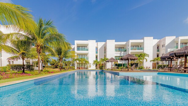 A swimming pool with a clear blue water surface, surrounded by white buildings and palm trees.