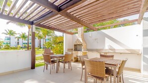 An outdoor patio with a wooden pergola, a brick oven, and wicker furniture.