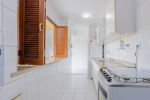 A kitchen with white tiled walls, a wooden door, a glass-top stove, and a white refrigerator.