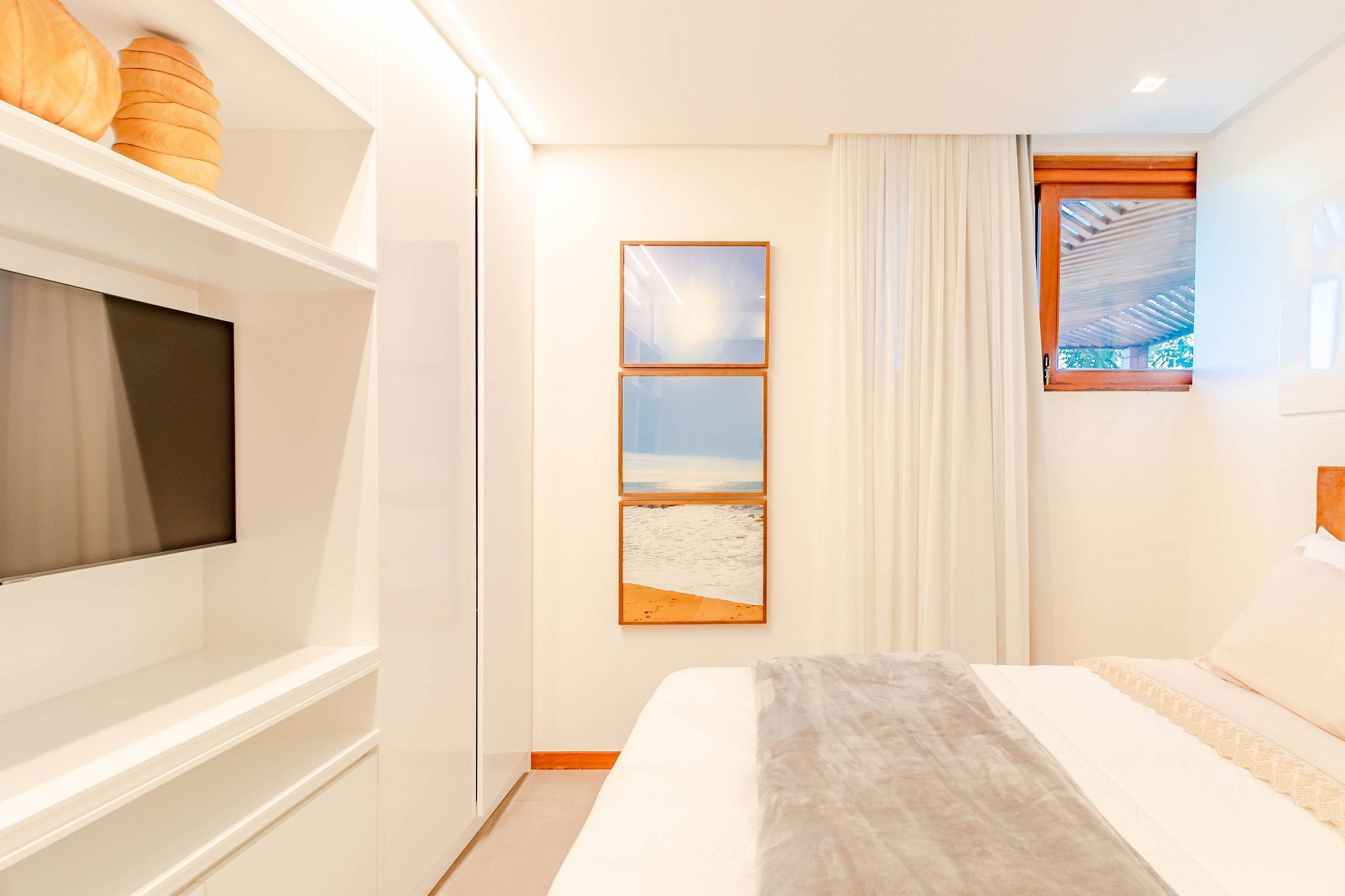 A modern bedroom with a bed, a TV, a window with curtains, and artwork on the wall.