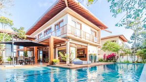 Ein modernes, zweistöckiges Haus mit Swimmingpool, Sitzgelegenheiten im Freien und einer überdachten Terrasse.