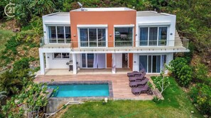 Une maison moderne à deux étages, dotée d’une piscine, de grandes fenêtres et d’un balcon.