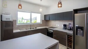 Una cocina moderna con armarios oscuros, un refrigerador de acero inoxidable, una cafetera y un lavavajillas.