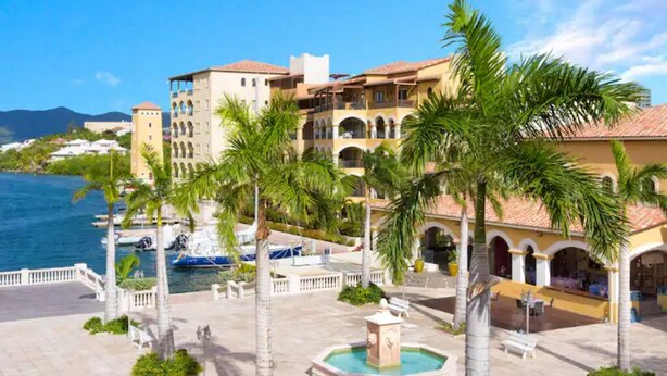 A hotel courtyard with palm trees, a fountain, and a view of the sea. - Porto Cupecoy- 3 Bedroom- Luxury Marina Penthouse (Sint Maarten)