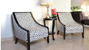 Two armchairs with a geometric pattern, a small table with a lamp, and a pink flower arrangement. - Porto Cupecoy- 3 Bedroom- Luxury Marina Penthouse (Sint Maarten)