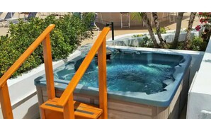 A hot tub with a wooden deck and orange railings, surrounded by greenery and a pool area. - Maho 1 bedroom condo beautifully decorated. (Sint Maarten)