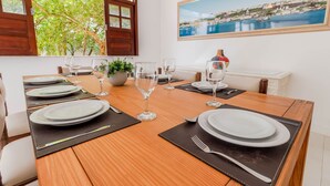 Een eettafel gedekt met borden, glazen en bestek, met uitzicht op een kustplaatsje door een raam.