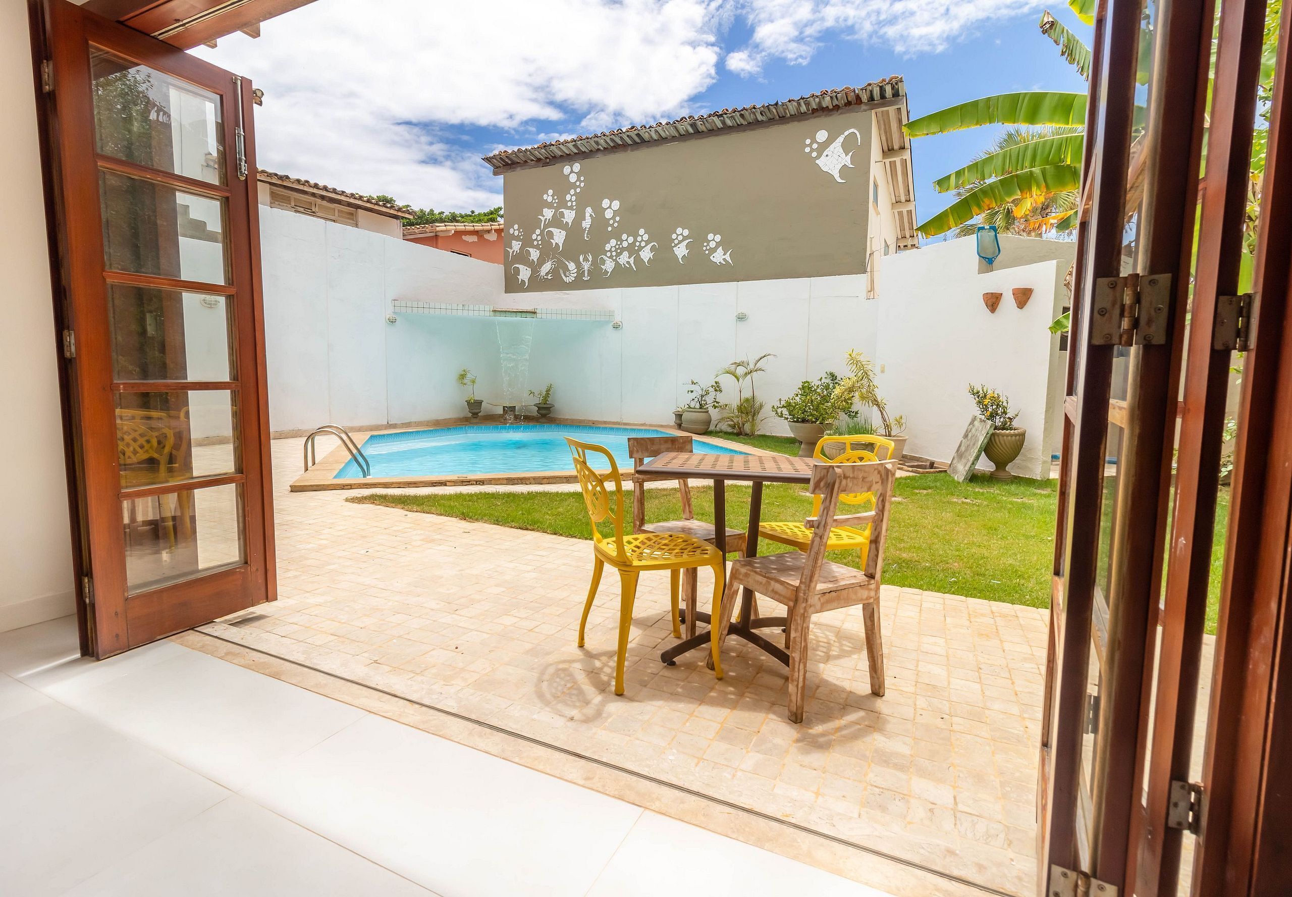 An outdoor patio with a pool, yellow chairs, and a table.