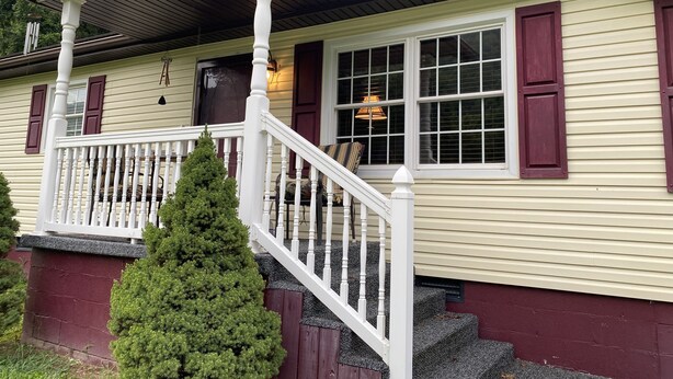 A two-story house with a front porch, a staircase, and a small tree in front. - A & B TRAIL HOUSE @ Hatfield-McCoy Trails, 5 Beds Plus Futon 2 Couches & 2 Baths (DELBARTON)